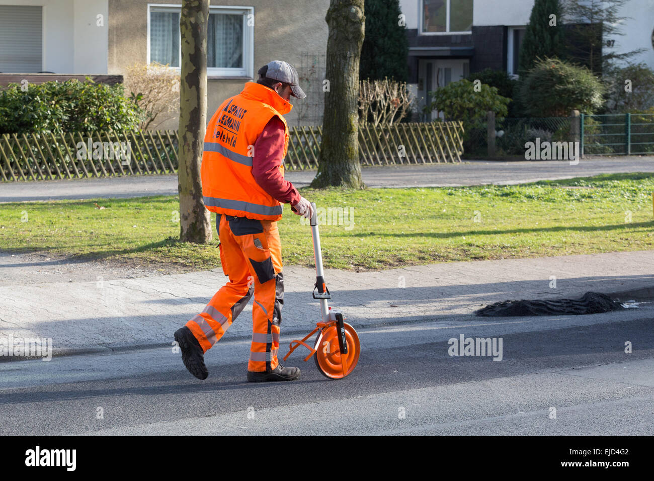 A man in fluorescent clothing uses a trundle wheel to measure a distance along a road Stock Photo