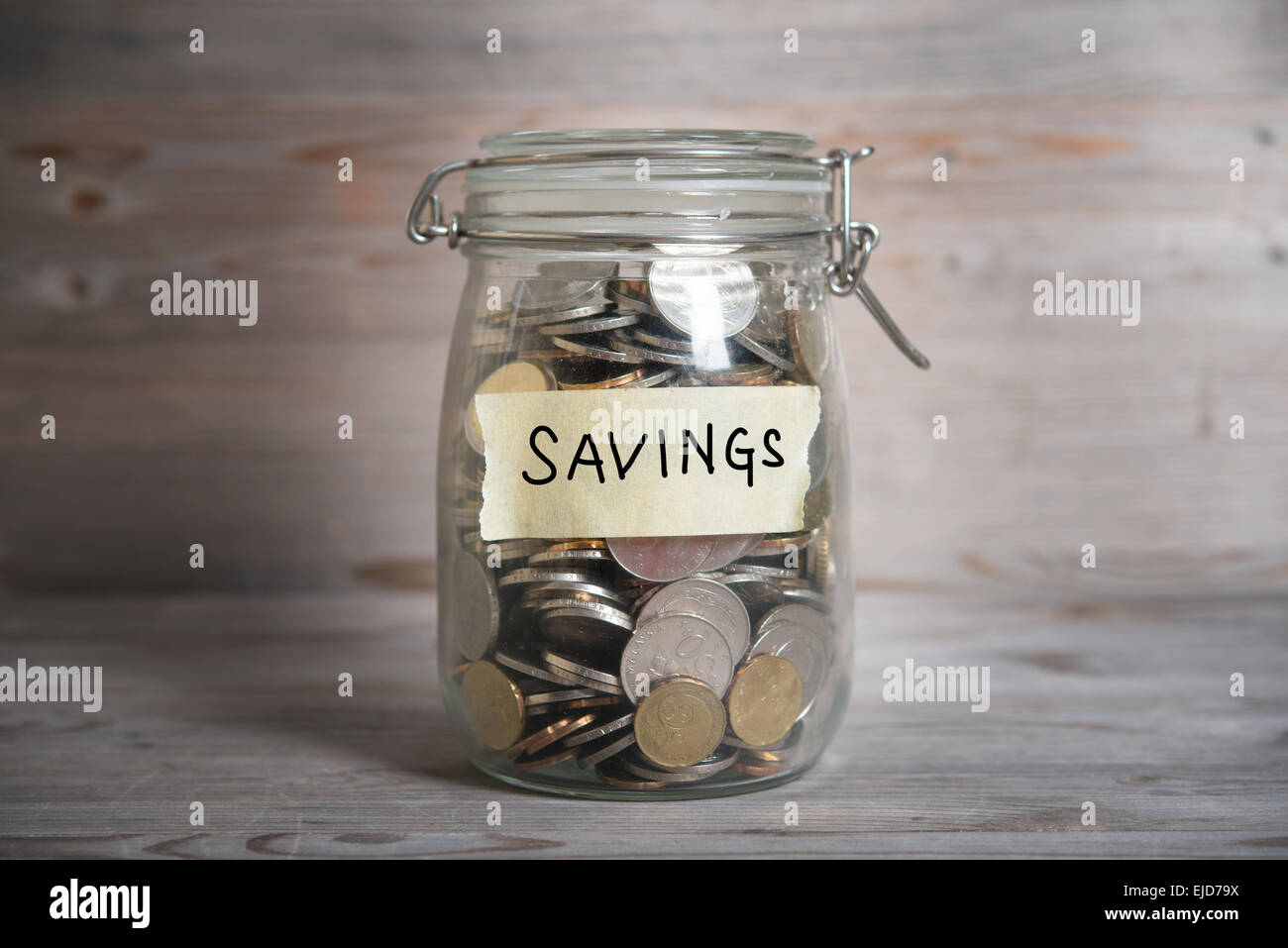 Coins in glass money jar with savings label, financial concept. Vintage wooden background with dramatic light. Stock Photo