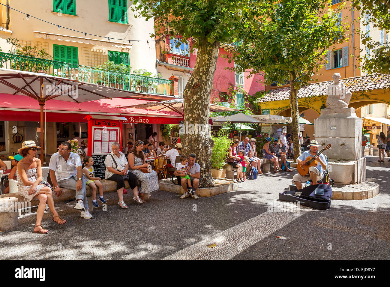 People listening to street musician on small square in old town of Menton, France. Stock Photo