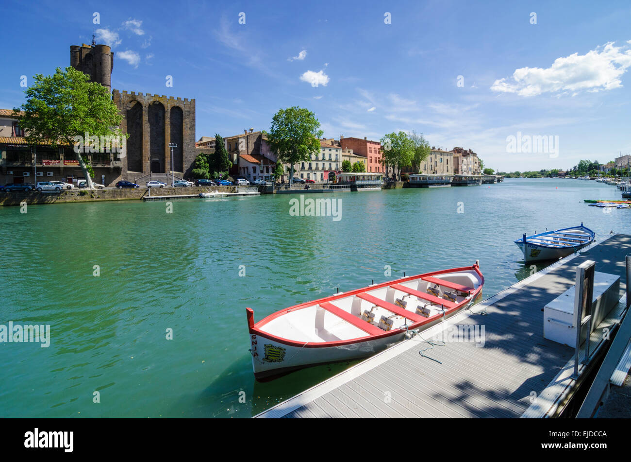 A small boat moored on the Herault River overlooked by Agde Cathedral in the town of Agde, Herault, Languedoc-Roussillon, France Stock Photo