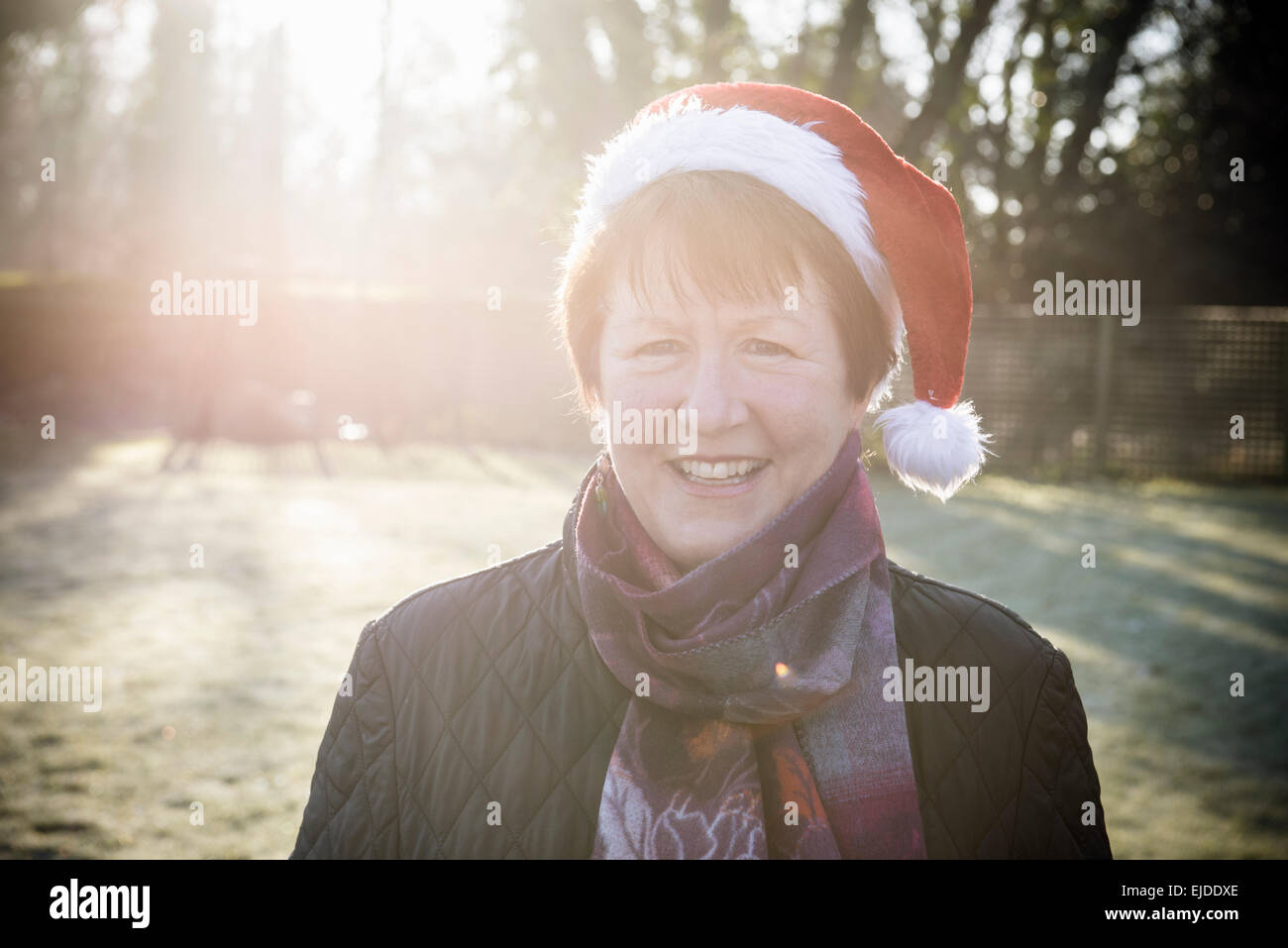 A woman standing in a garden, wearing a red Christmas Santa hat. Stock Photo