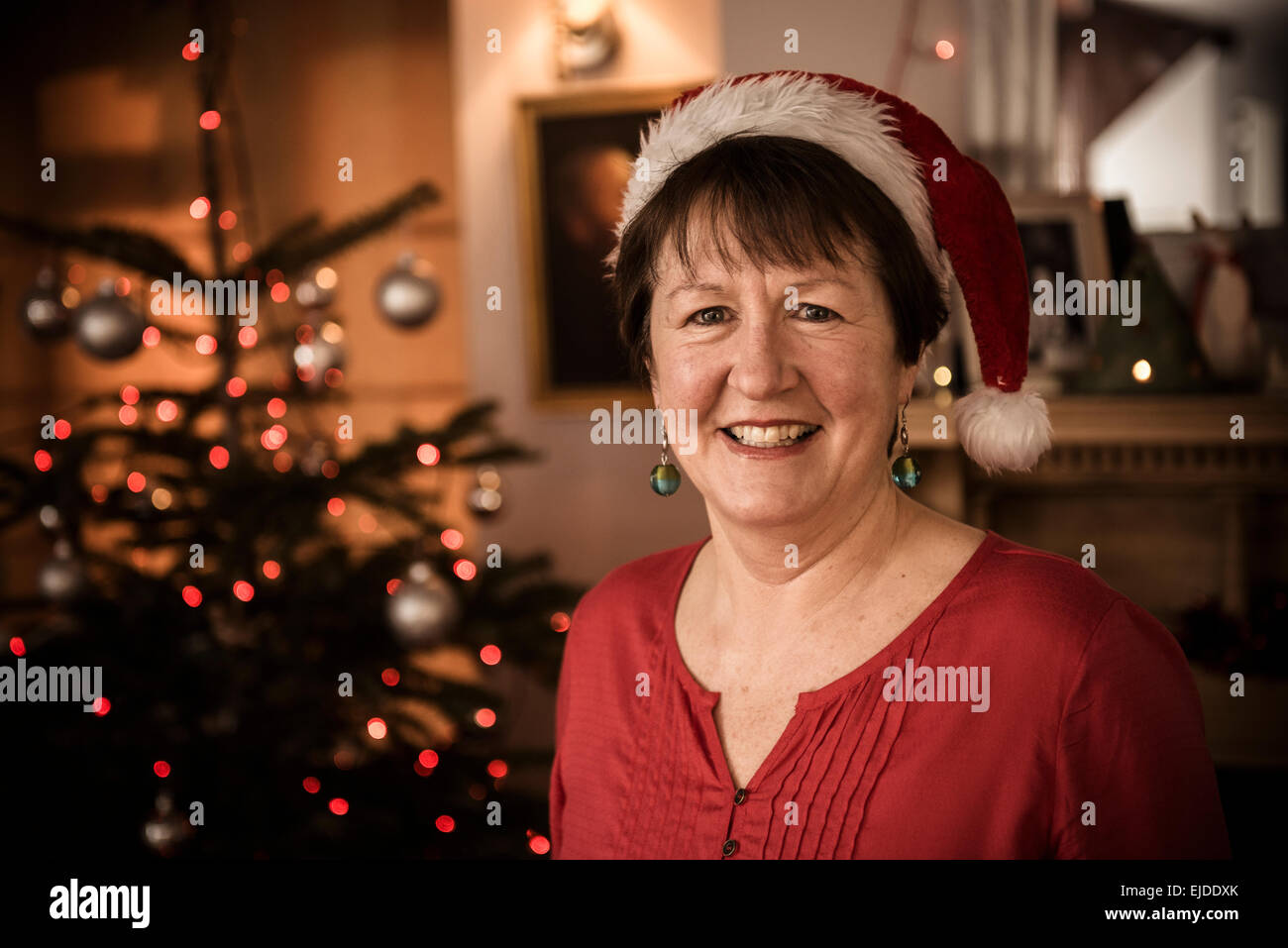 A woman by a Christmas tree wearing a Santa hat. Stock Photo