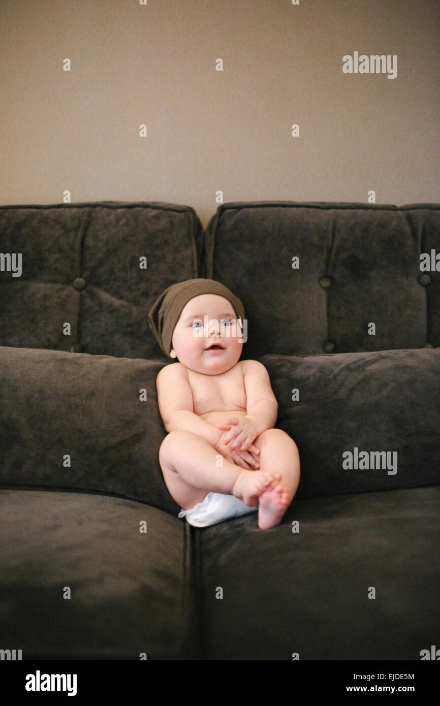 A baby sitting propped up on a sofa wearing a diaper Stock Photo Alamy