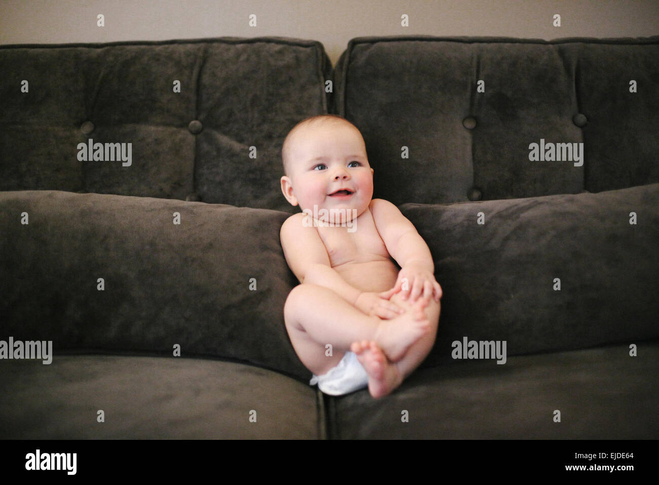 A baby sitting propped up on a sofa wearing a diaper Stock Photo Alamy