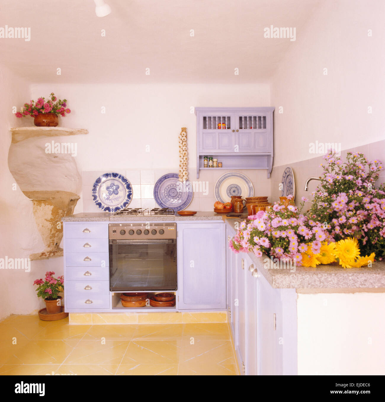 Fresh flowers on worktop in small rustic Mallorcan kitchen with mauve painted units Stock Photo