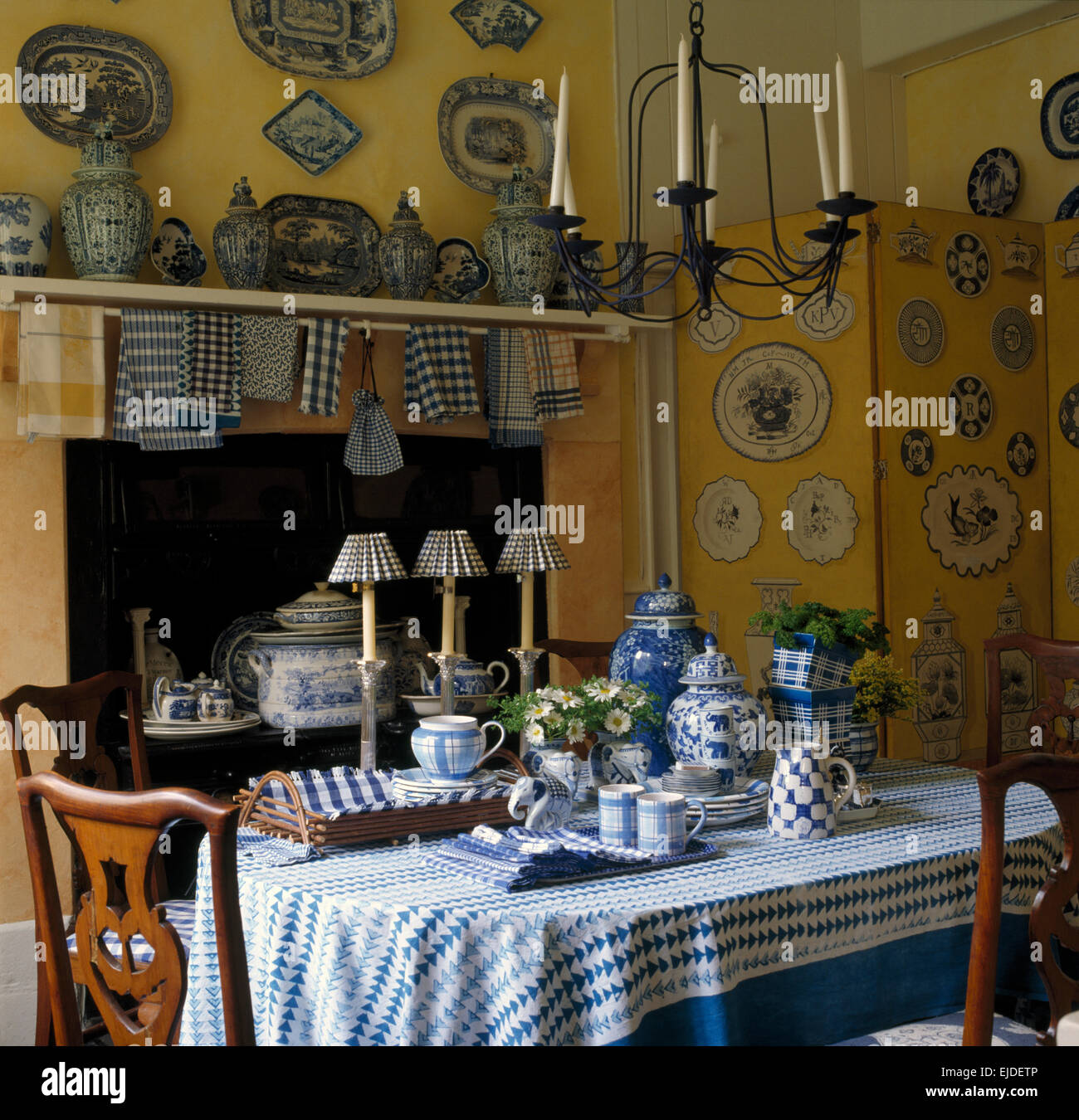 Collection of blue+white china on shelf in yellow nineties kitchen with blue patterned cloth on dining table Stock Photo