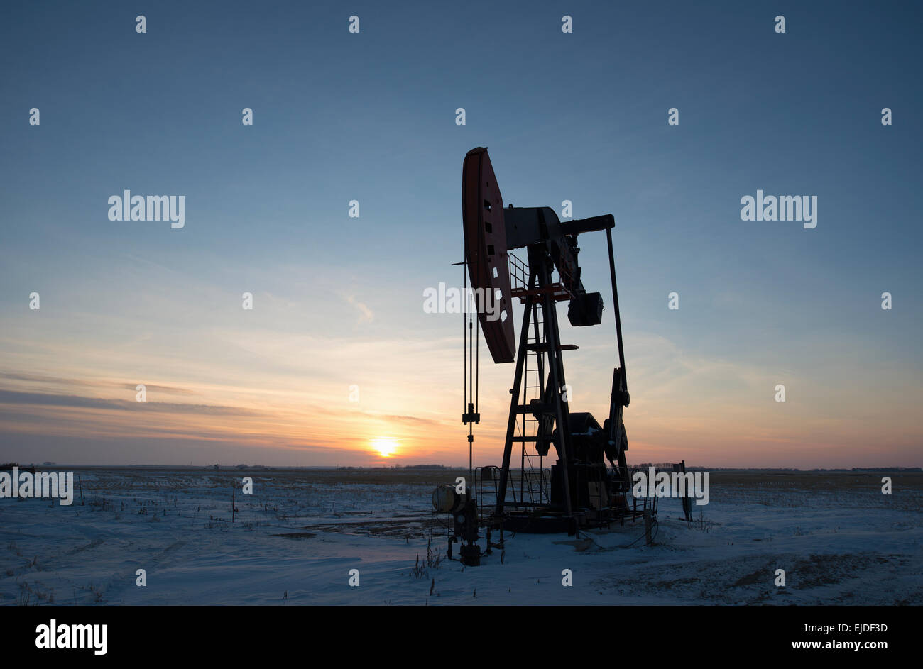 An oil drilling rig and pumpjack on a flat plain in the Canadian oil ...