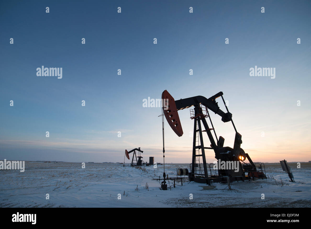 An oil drilling rig and pumpjack on a flat plain in the Canadian oil ...