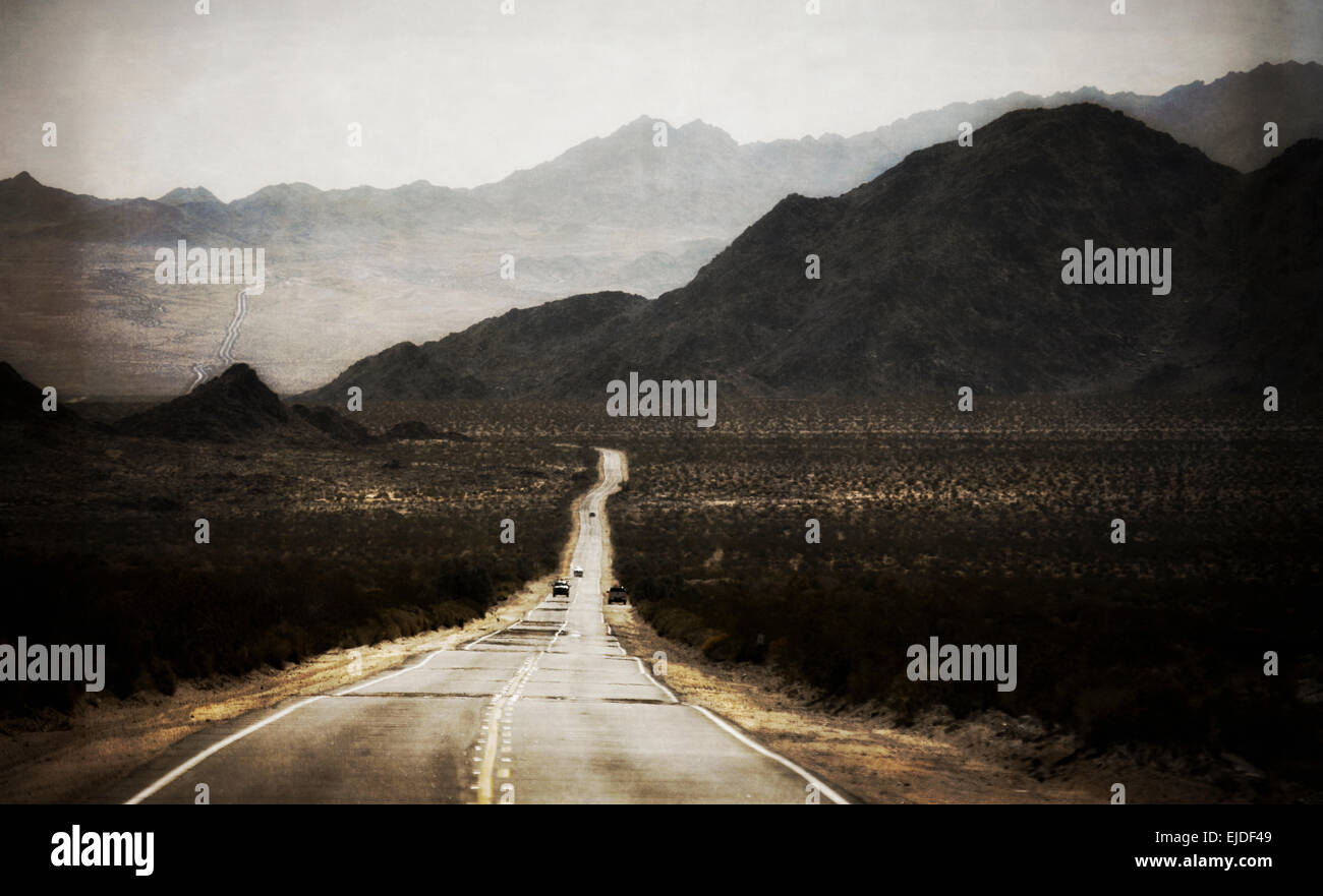A road leading into the distance, to a range of mountains. Desert scenery, cars on the road. Stock Photo