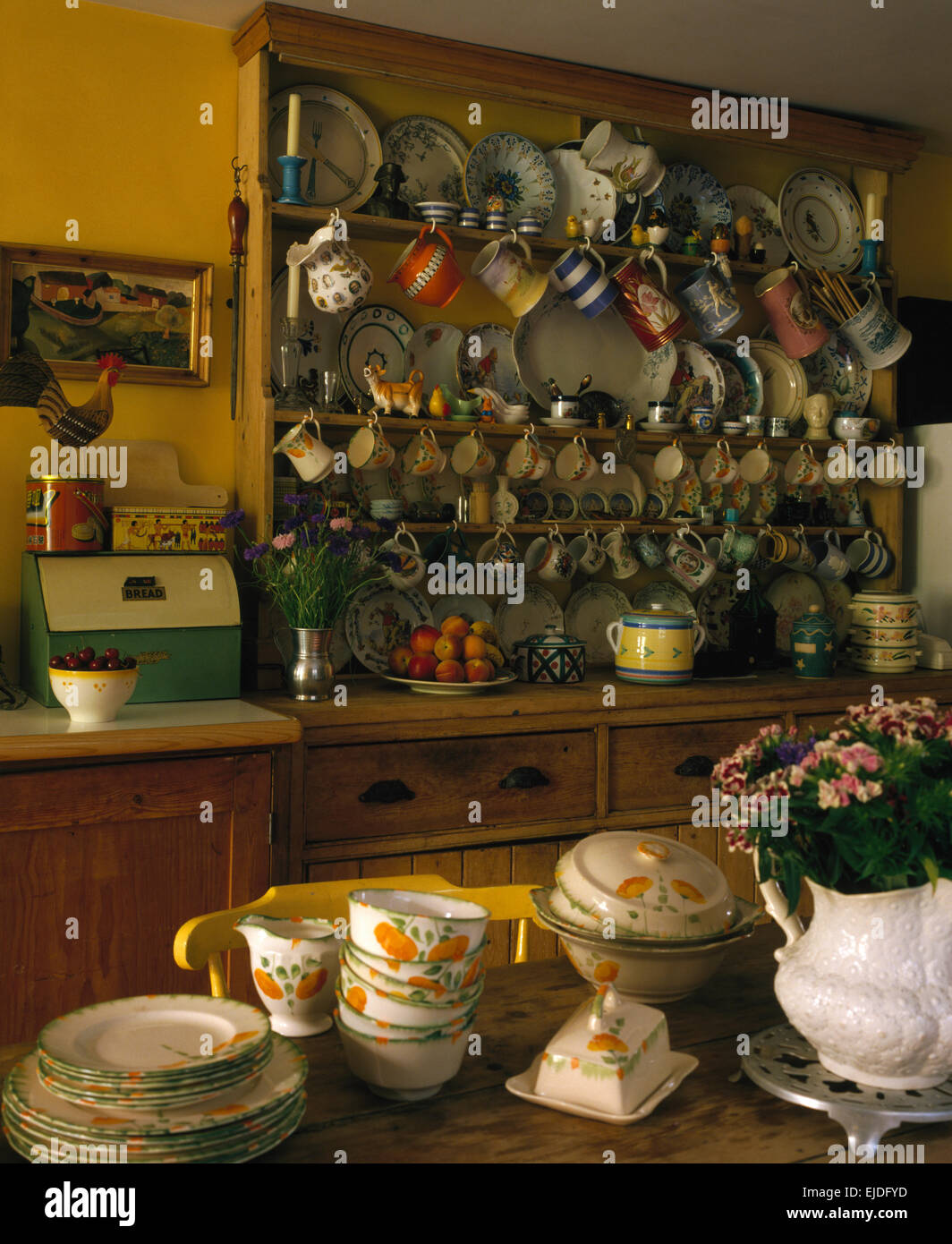 Vintage crockery on table in yellow eighties kitchen with collection of pottery on pine dresser Stock Photo