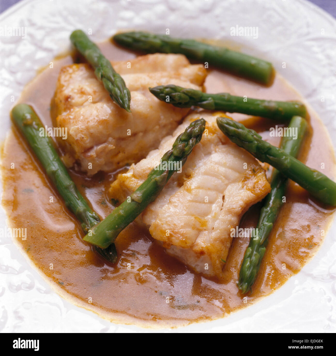 Close-up of roasted cod in a piquant sauce with asparagus Stock Photo
