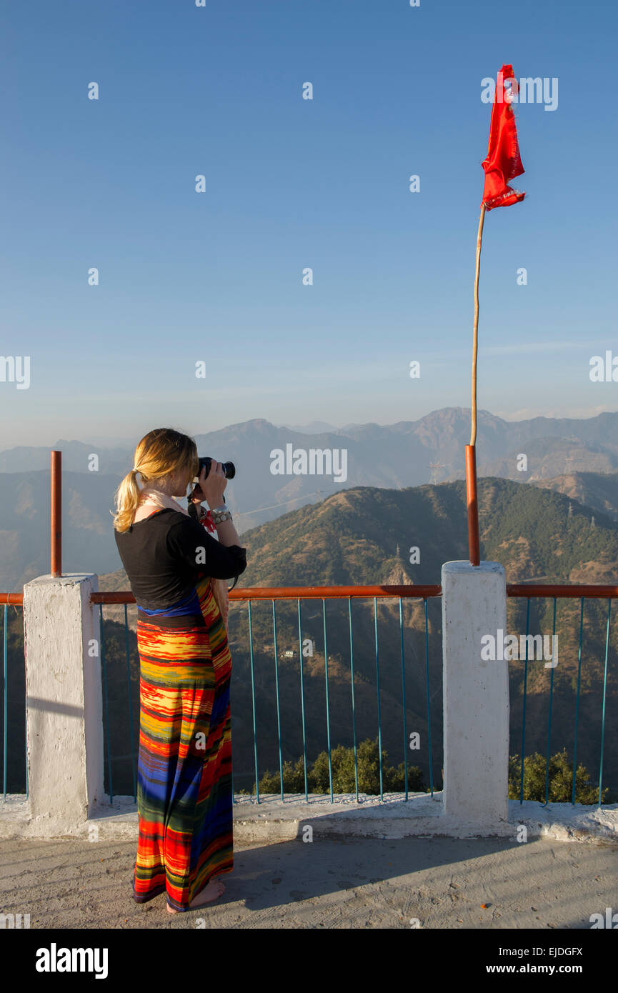 A female tourist in a brightly coloured dress taking photos from Kunjapuri Temple near Rishikesh, India, overlooking the Himalayas at sunset Stock Photo