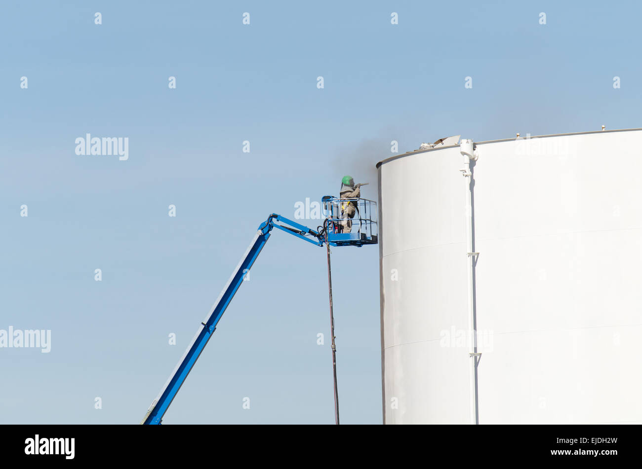 Worker sandblasting petroleum storage tank prior to painting Stock Photo