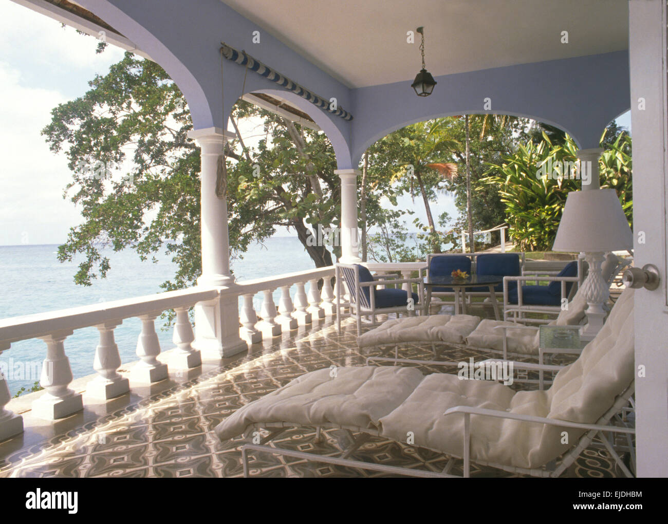Loungers on tiled veranda of Caribbean villa overlooking the ocean Stock Photo