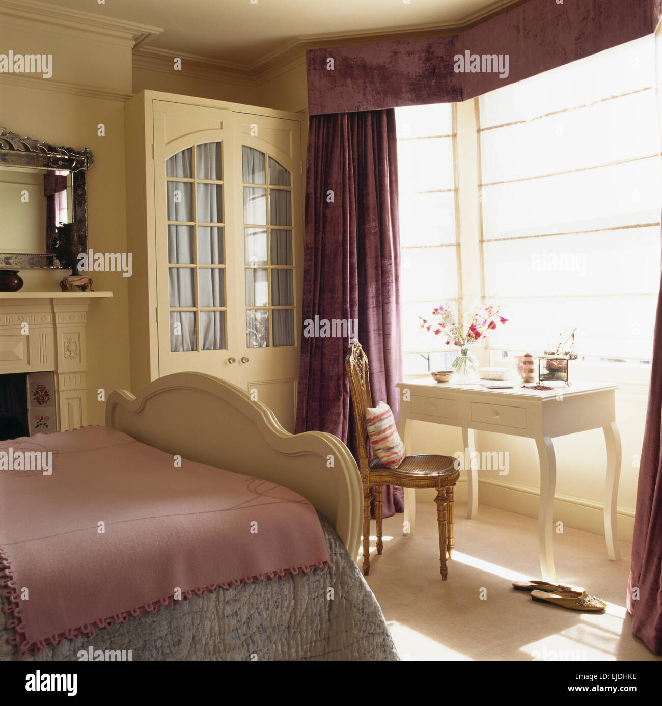 Cream fitted wardrobe with interior drapes in traditional bedroom with purple curtains and fine linen blinds on the window Stock Photo