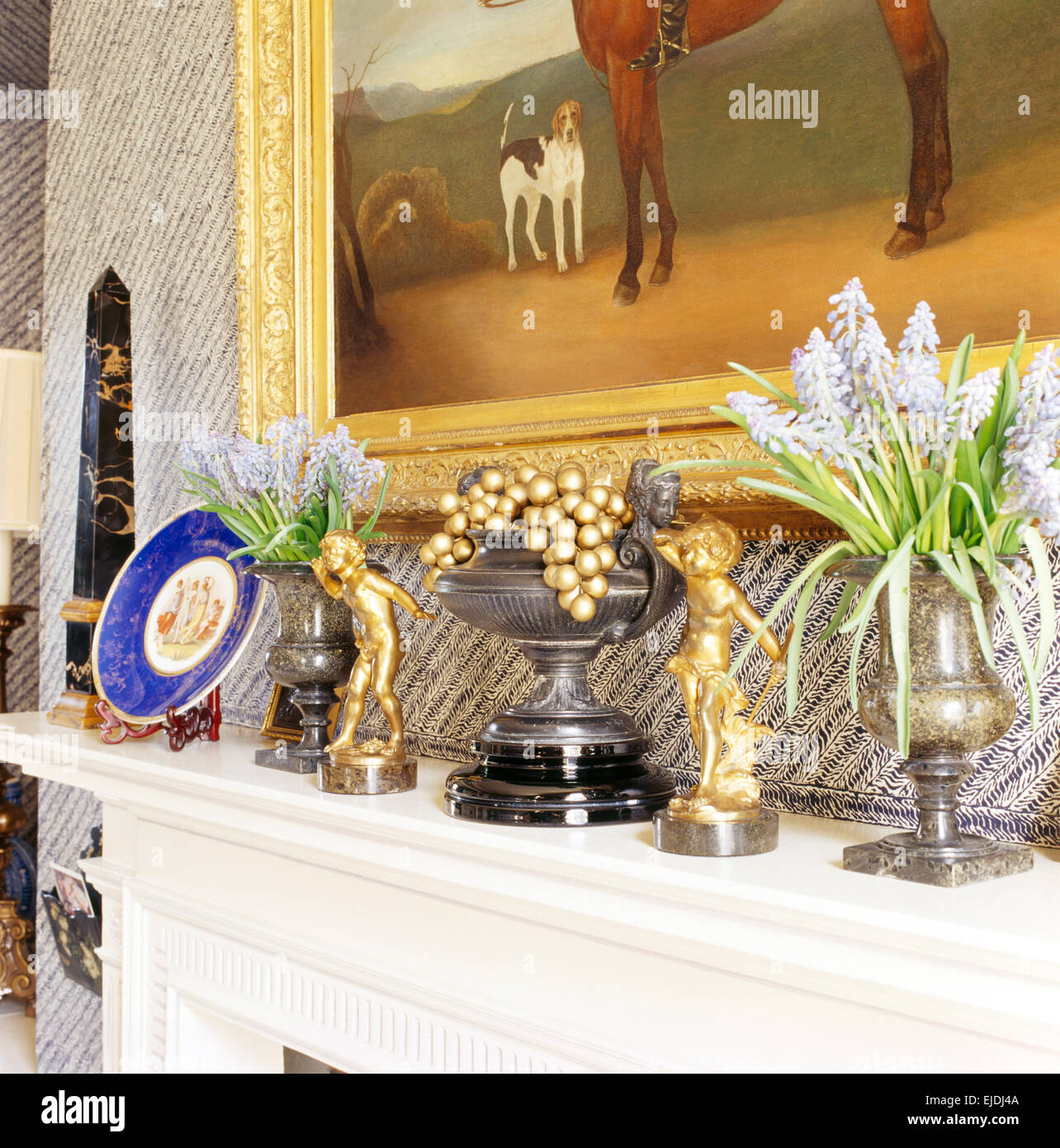 Close-up of small gold statues on mantelpiece with vases of pale blue grape hyacinths Stock Photo