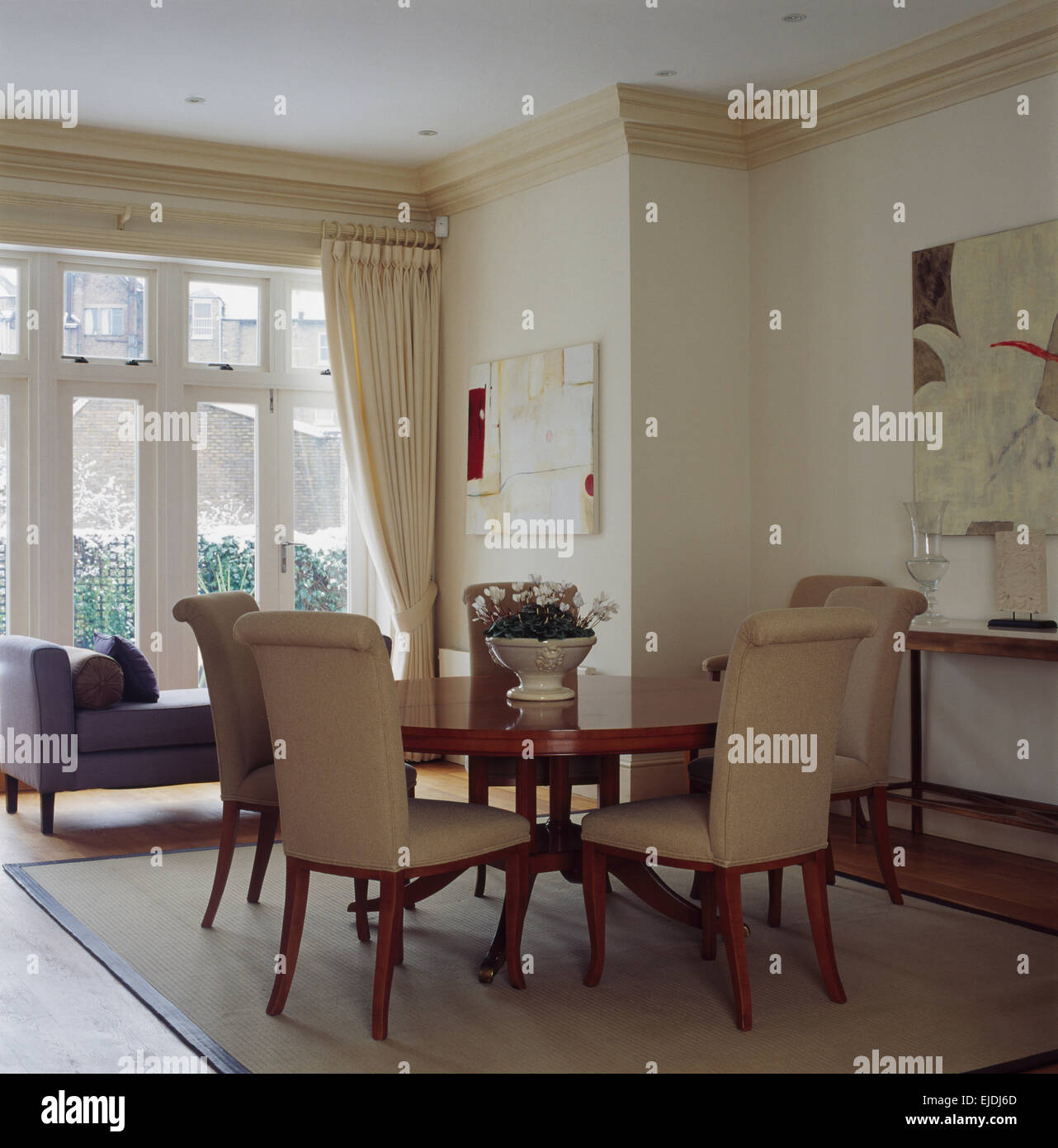 Cream upholstered chairs at circular table in light and airy contemporary dining room with cream