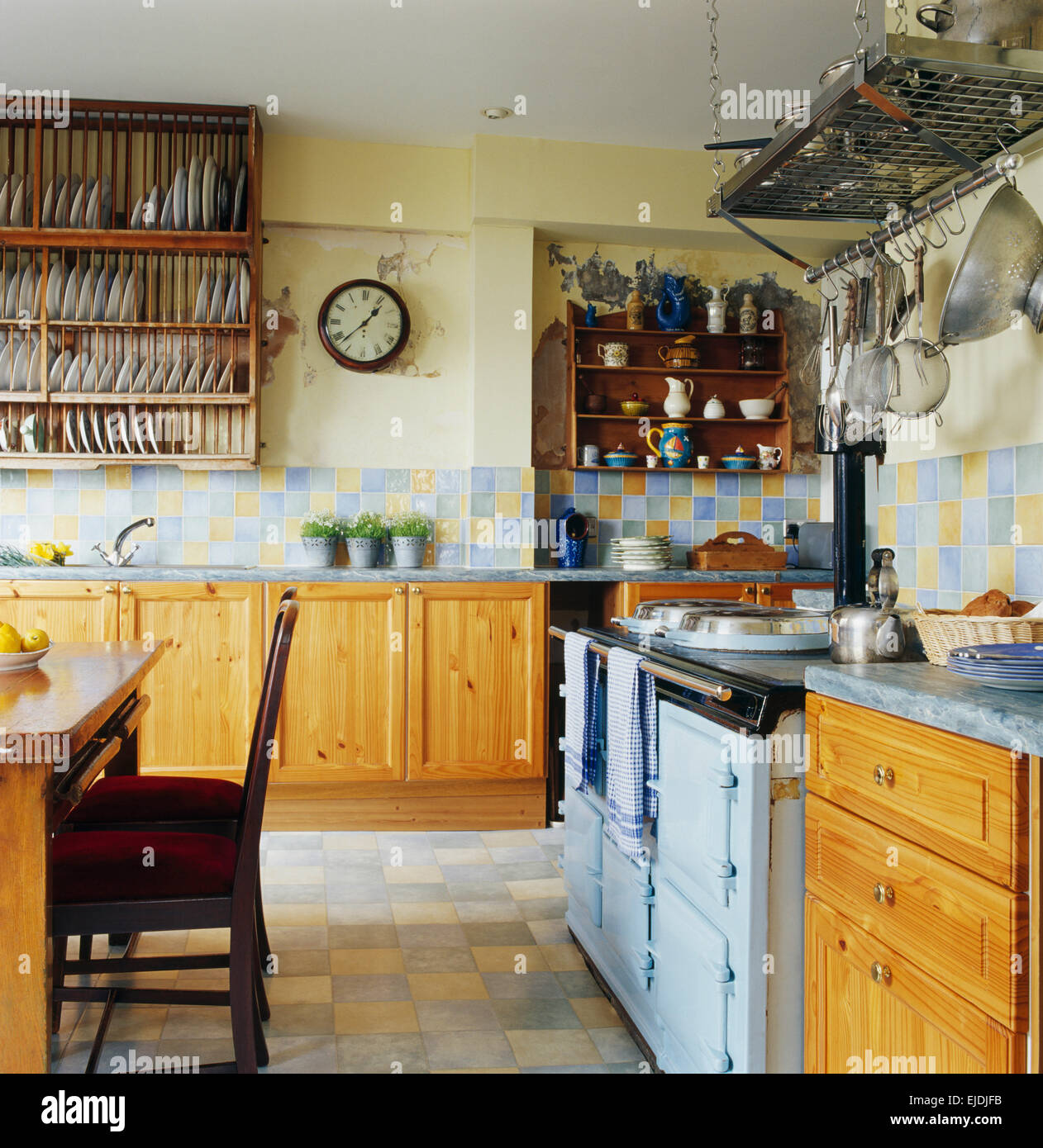 Pine units and pale blue Aga in traditional coastal kitchen with  blue+yellow tiling and a large pine plate rack Stock Photo - Alamy