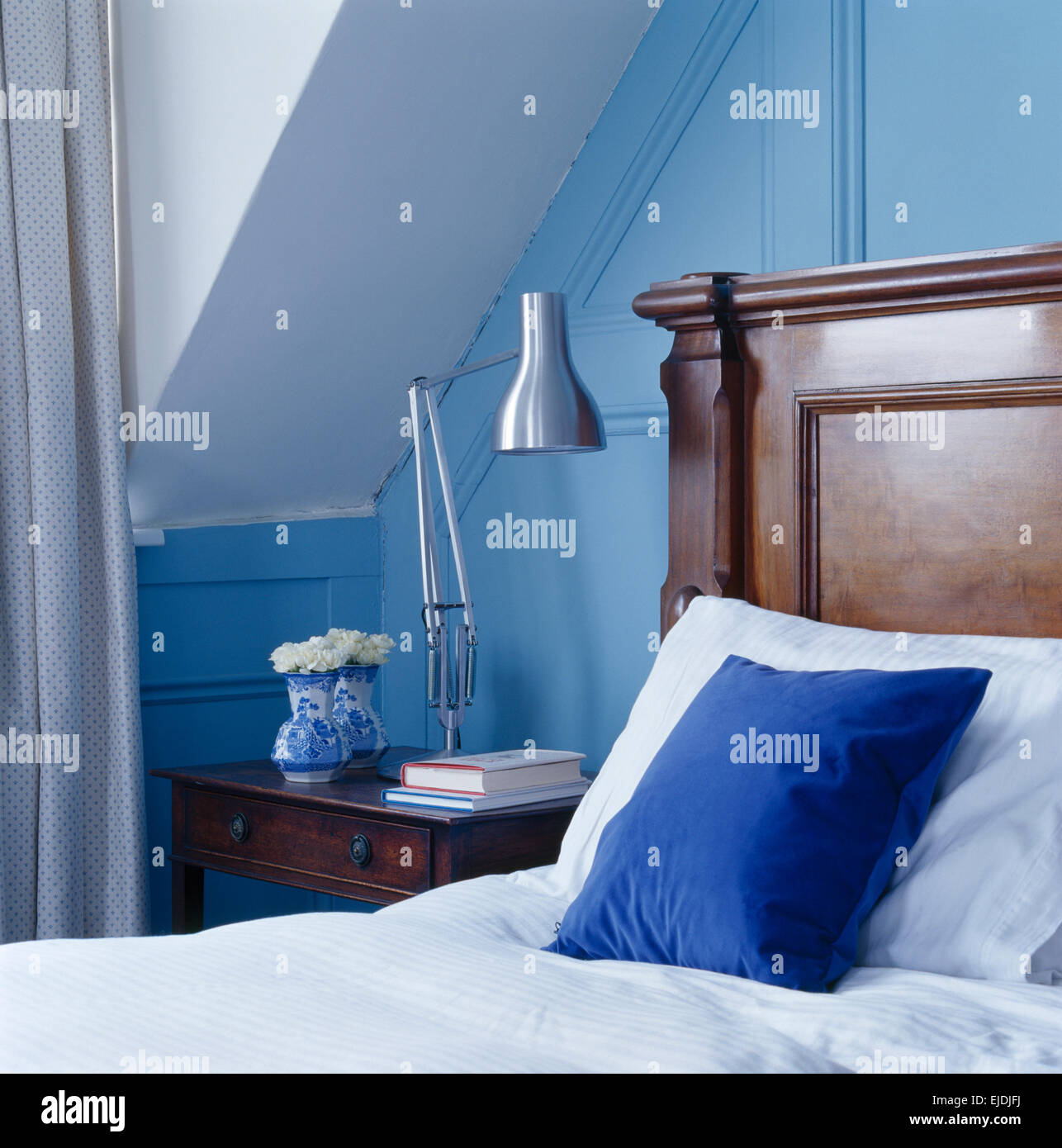 Chrome lamp on low table beside mahogany bed with bright blue cushion in pale blue bedroom Stock Photo