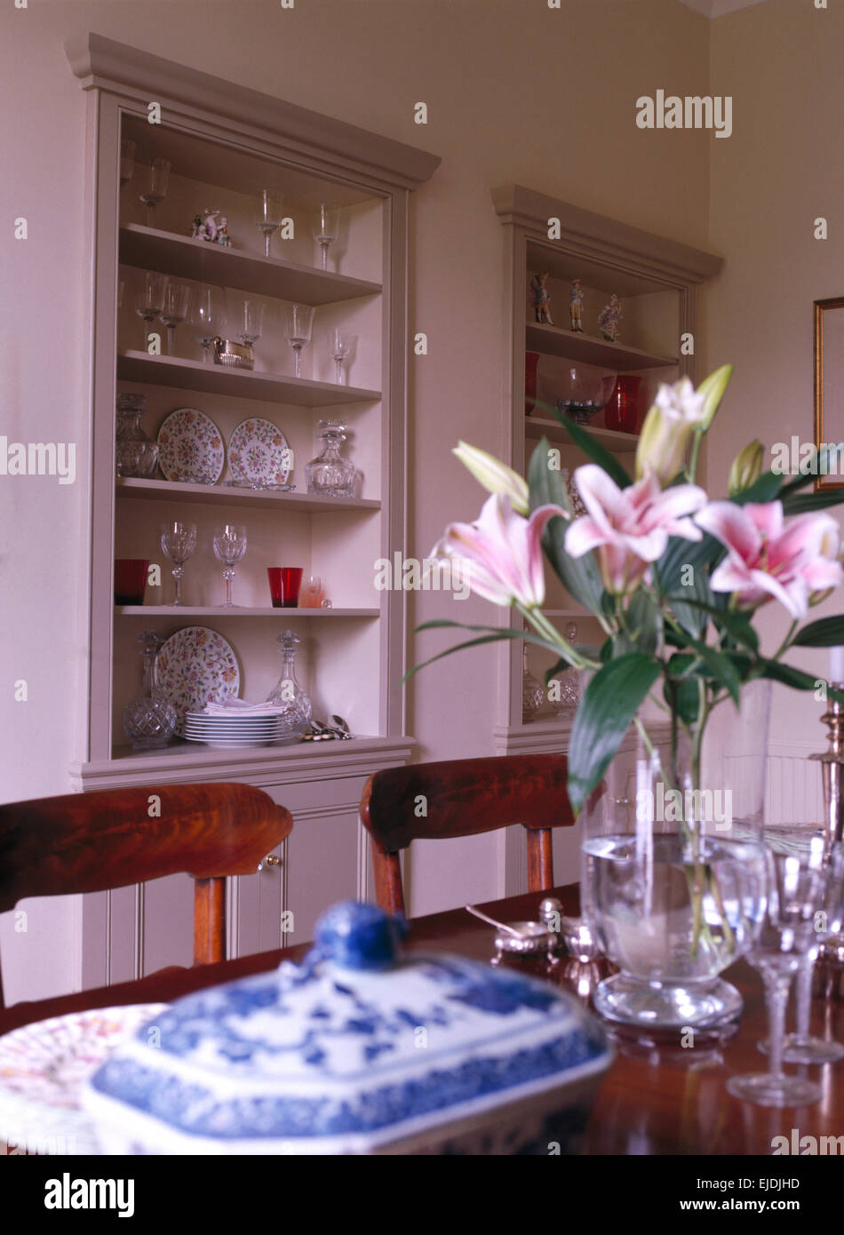 Vase of pink lilies on table set for lunch in traditional dining room with alcove shelving Stock Photo