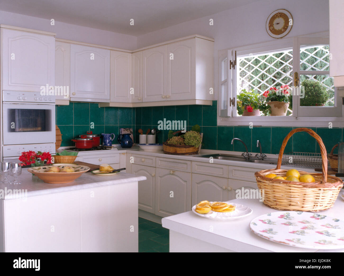 White fitted units in coastal kitchen with green tiled splash back and basket of lemons on worktop Stock Photo