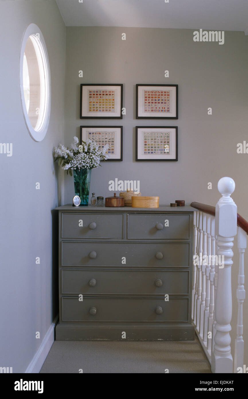 Pale gray painted chest of drawers on narrow country landing with white painted banisters Stock Photo