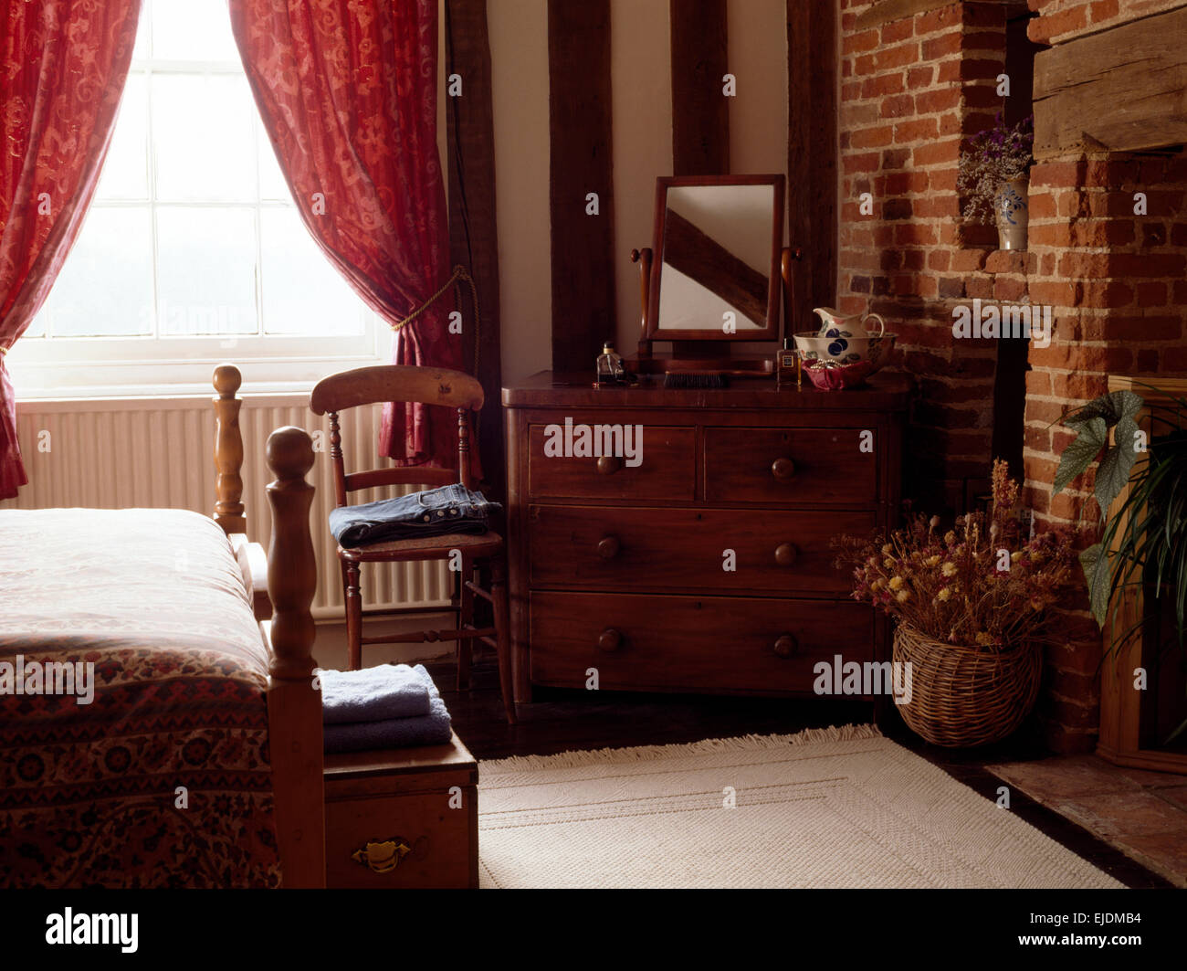 Victorian mahogany chest of drawers in nineties cottage bedroom with exposed brick wall Stock Photo