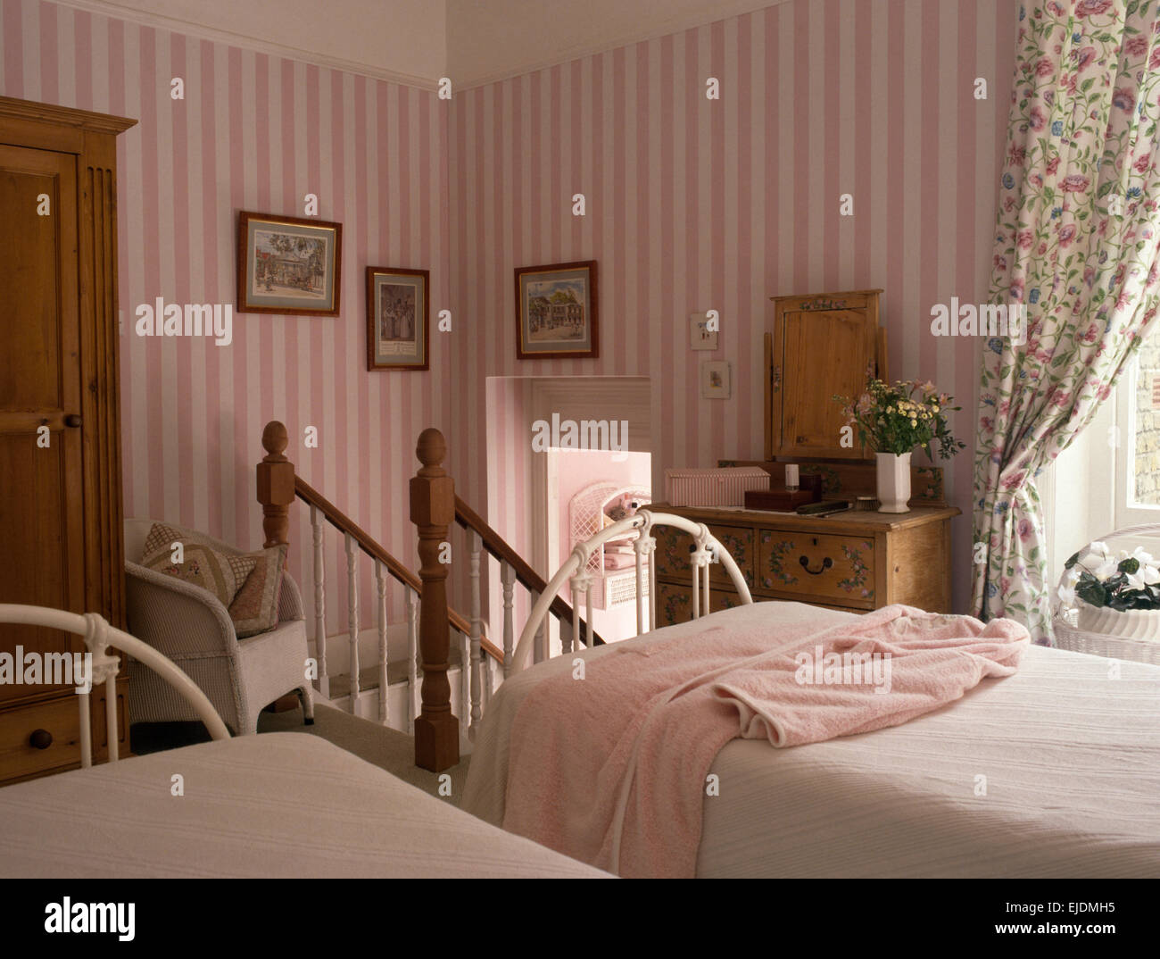 Pink striped wallpaper in country bedroom with white wrought iron twin beds Stock Photo