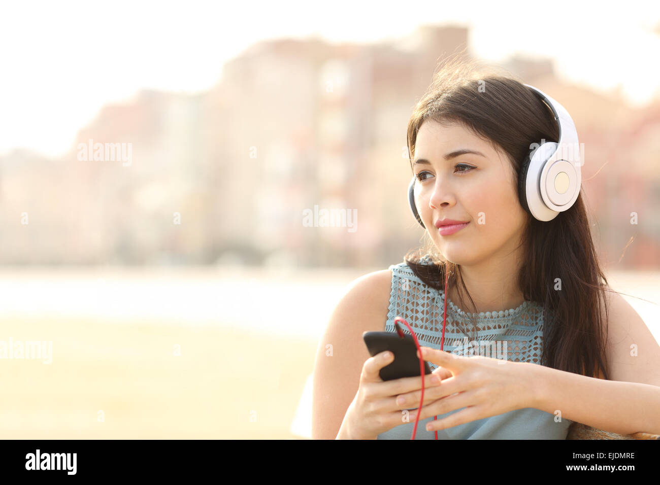 Candid girl thoughtful and listening to the music with a smart phone and looking away Stock Photo