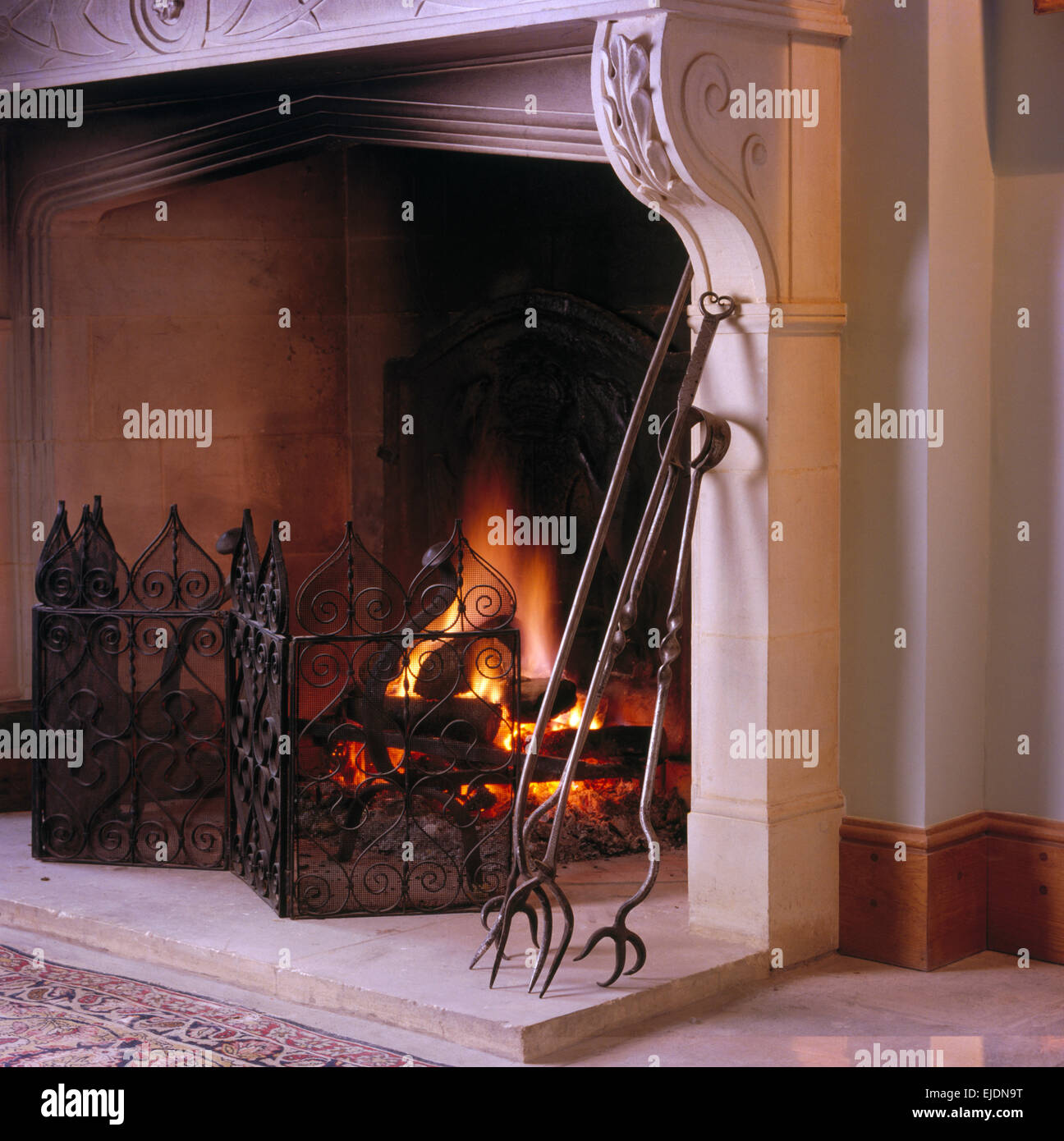 Close-up of fireplace with lighted fire and wrought iron fireguard and fire tongs Stock Photo