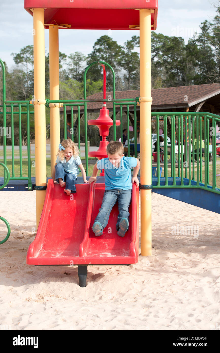Young boy and girl go down slide in park playground Stock Photo