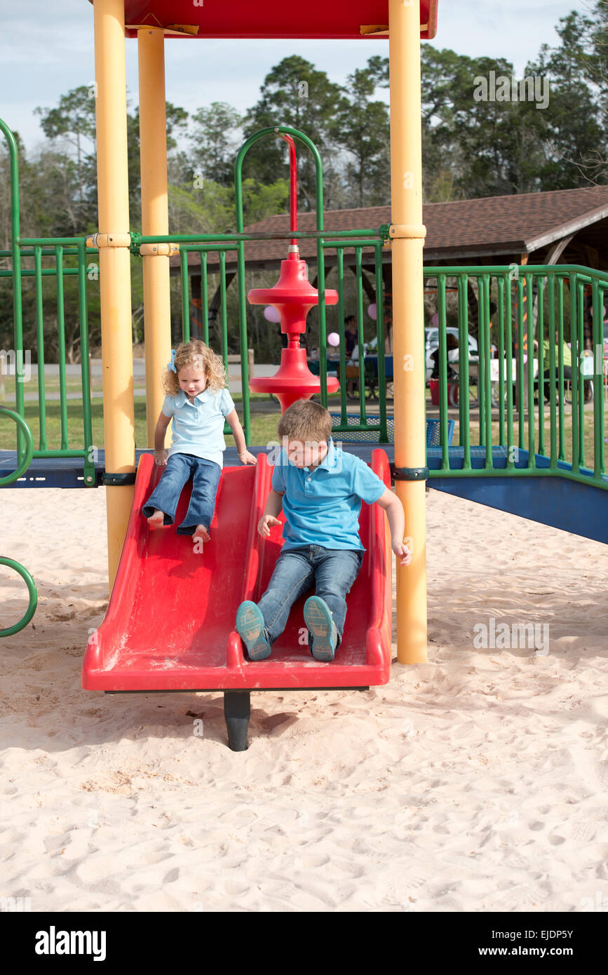 Young boy and girl go down slide at park playground Stock Photo