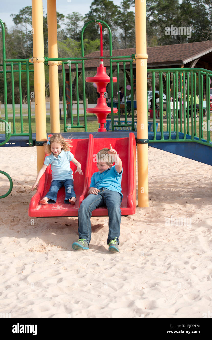 Young boy and girl going down slide in park playground Stock Photo