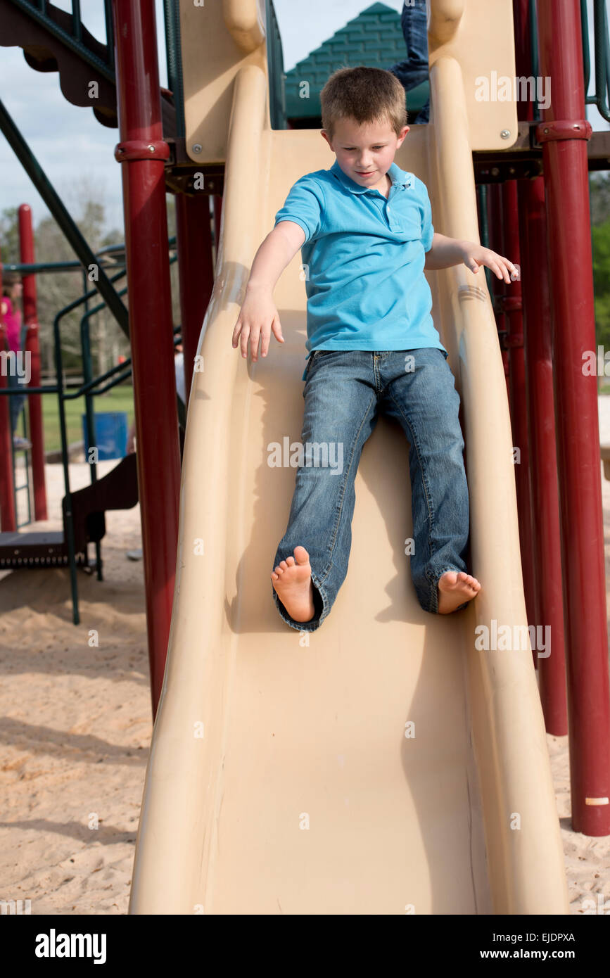 Eight year old boy sliding on park playground Stock Photo