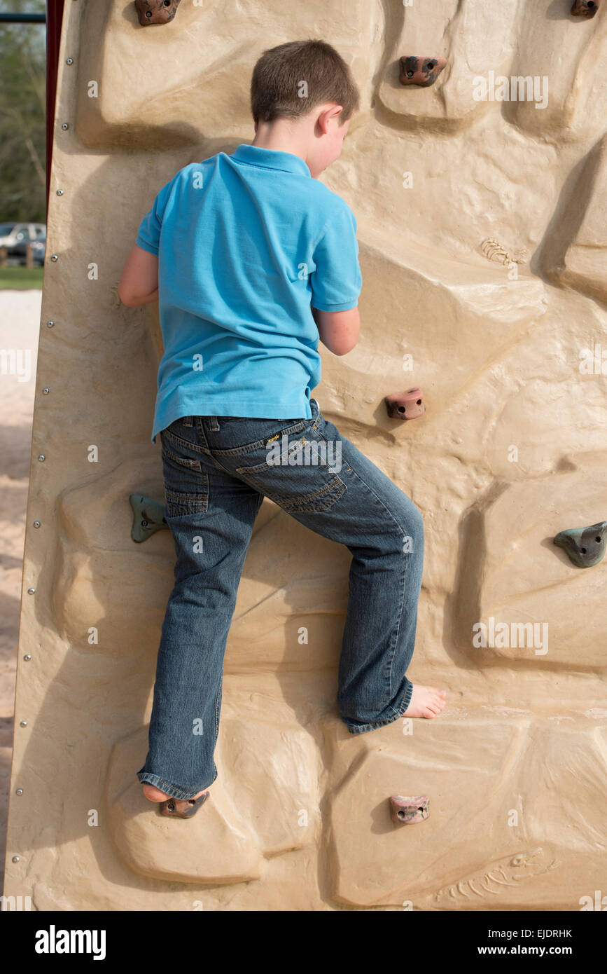 Eight year old boy climbing rock wall at park playground Stock Photo