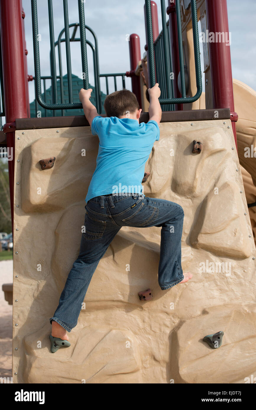 Eight year old boy climbing rock wall at park playground Stock Photo