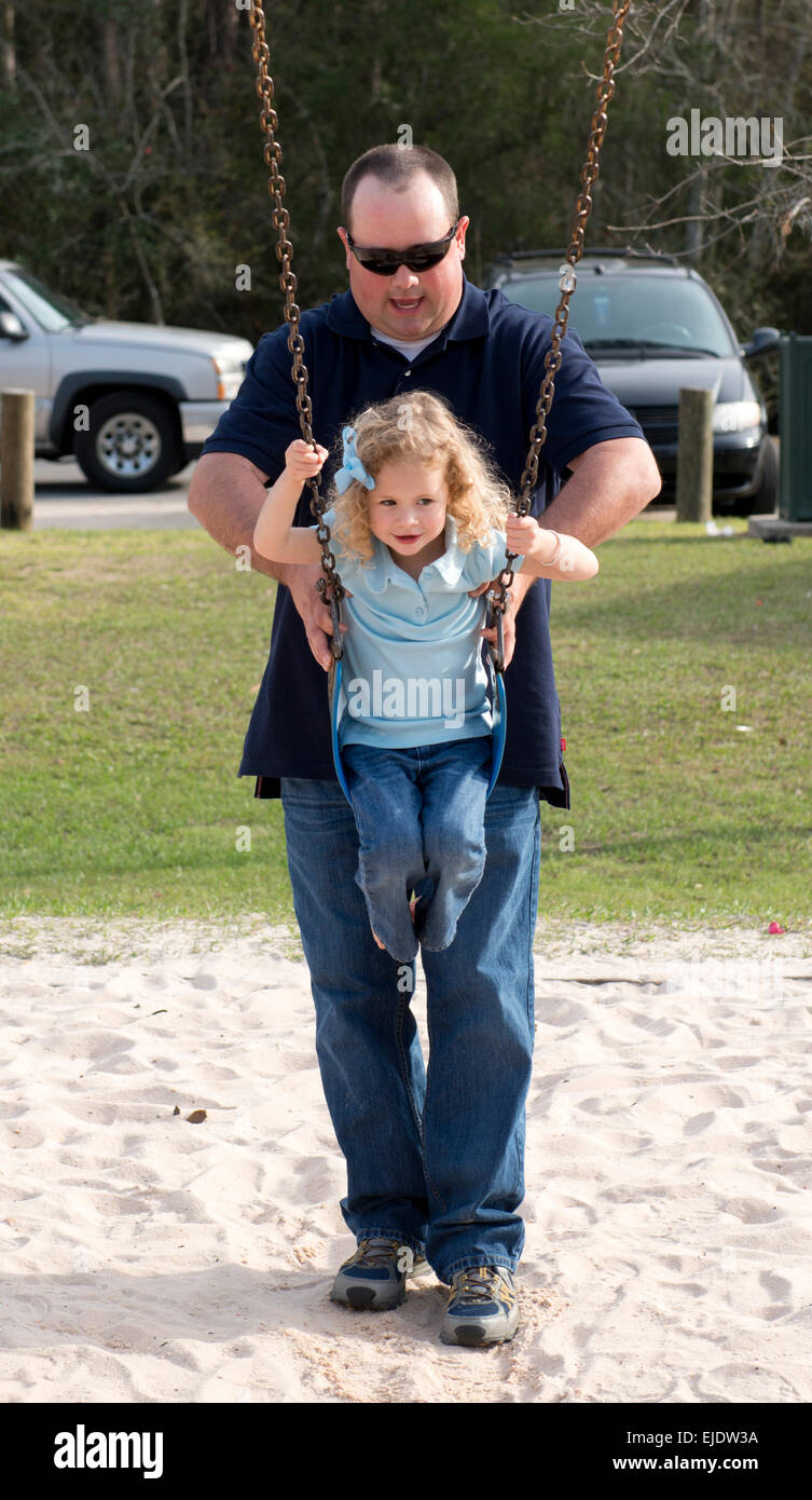 Father giving daughter a push on a swing at a park playground Stock Photo