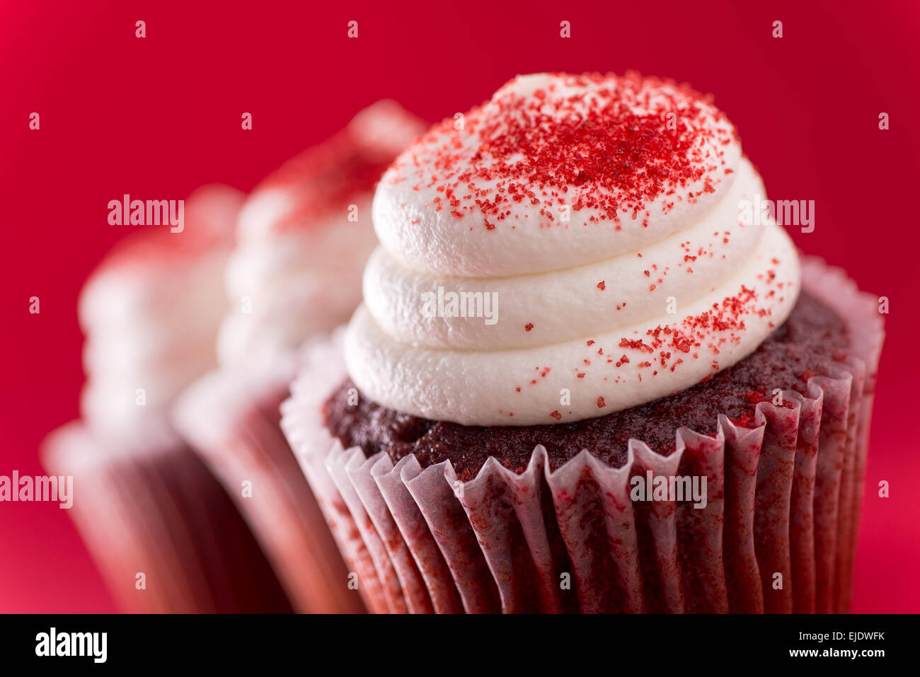 Three delicious red velvet cupcakes against a red background. Stock Photo