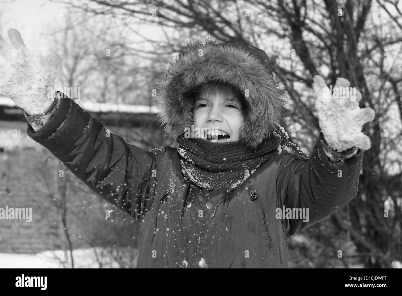 Black and white photo of preschool girl with auburn hair and brown eyes is playing with snow outside in a winter day. He is dres Stock Photo
