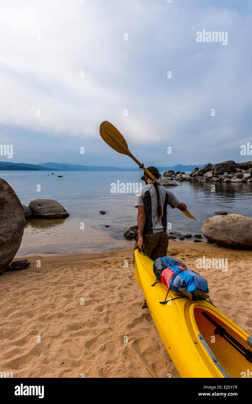 Man with a paddle over his shoulder dragging a kayak. Stock Photo