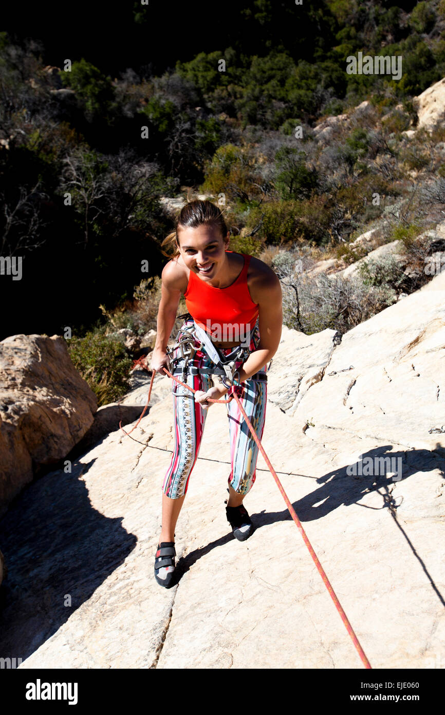 A woman wearing a red tank top and striped pants rappels Lower Gibraltar Rock in Santa Barbara, California. Stock Photo