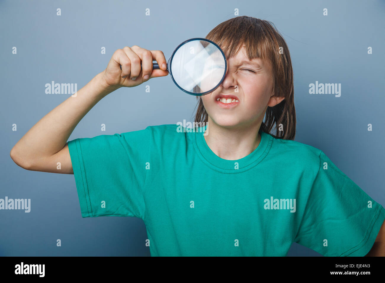 European-looking boy of ten years holding a magnifying glass, a keen eye on gray background Stock Photo