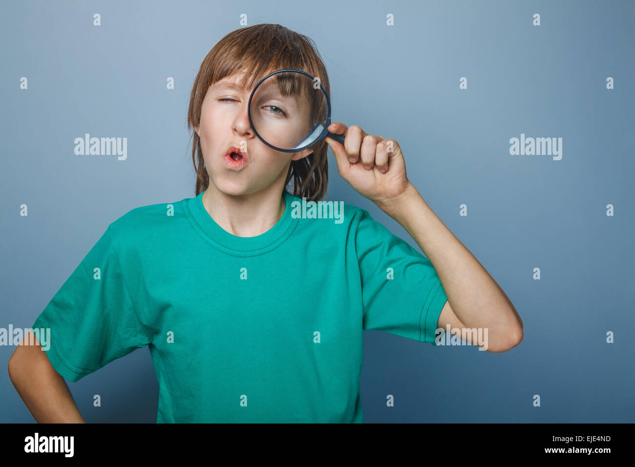 European-looking boy of ten  years holding a magnifying glass, a keen eye on gray background Stock Photo