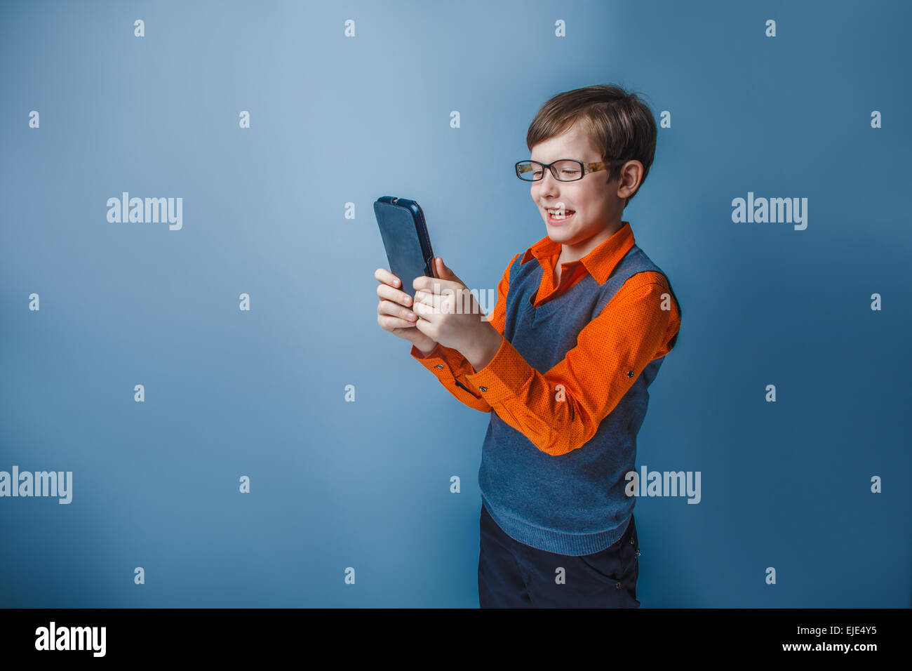 European-looking boy of ten years in glasses holding tablet in hand, plays, pleasure on a blue background Stock Photo