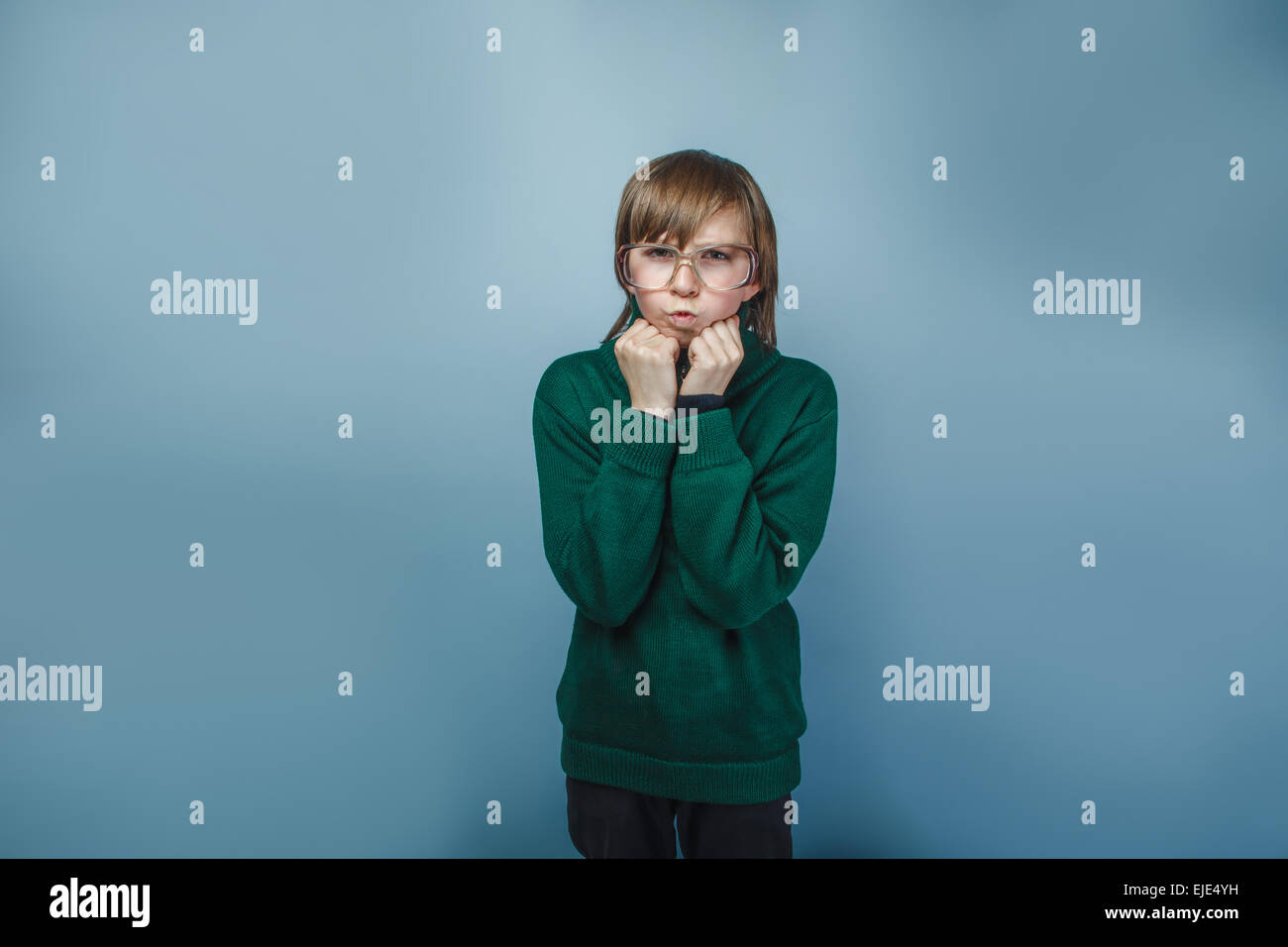 teenager boy with glasses lips blowing antics emotions fists in the face on a blue background Stock Photo