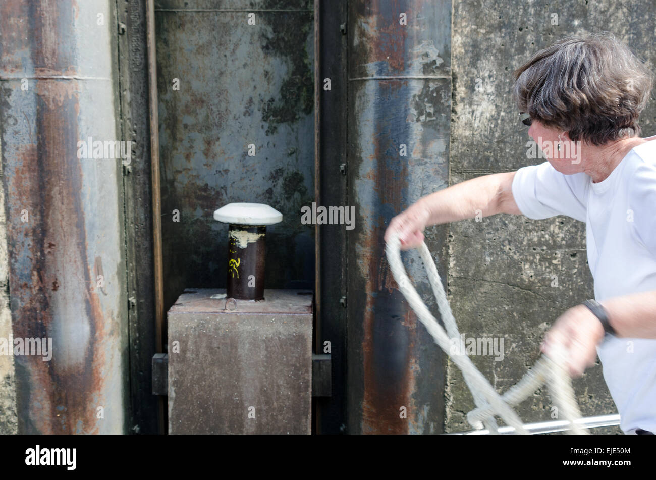 A woman tosses a line around a floating bollard as she prepares to take her boat through a lock on the Canal du Centre, France. Stock Photo