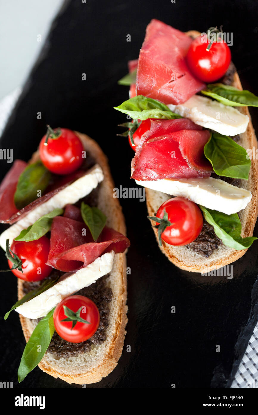 Toasts with tomato, ham, basil and eggplant puree Stock Photo