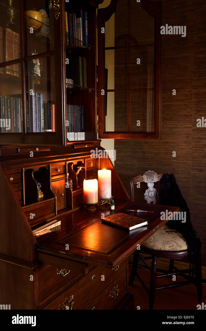 Glow of candles on antique mahogany secretary writing desk in moody dark room with chair Stock Photo