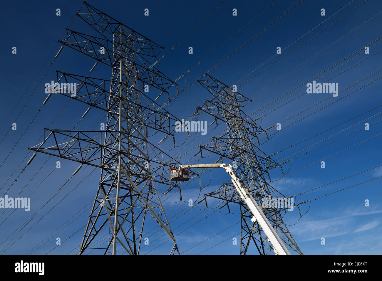 Hydro linemen on large cherry picker working on a double circuit high tension power line steel towers Toronto with blue sky Stock Photo