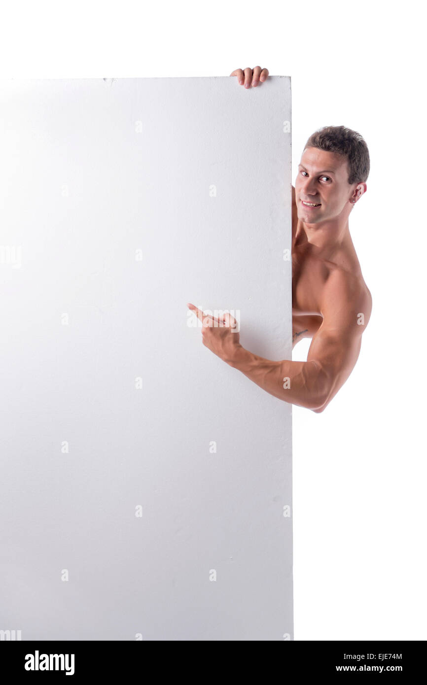 Strong muscular young man behind a blank vertical white banner looking at camera, pointing at the copyspace for your text, on wh Stock Photo